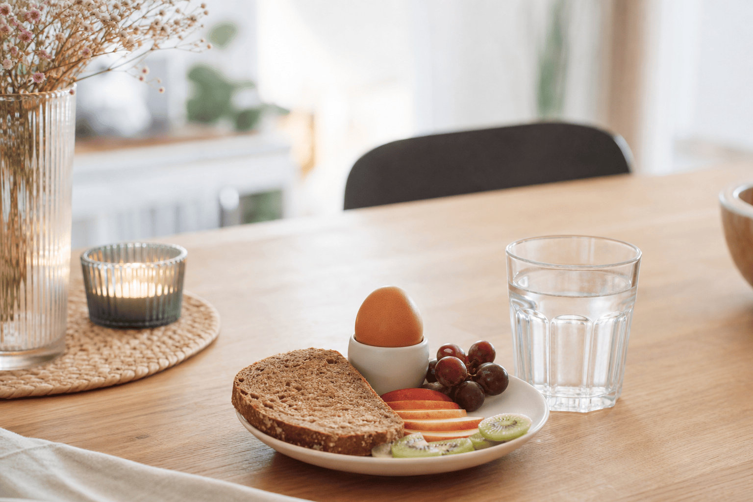 Kleine ausgewogene Mahlzeit mit Brot, Ei, Obst und Wasser auf einem Esstisch.