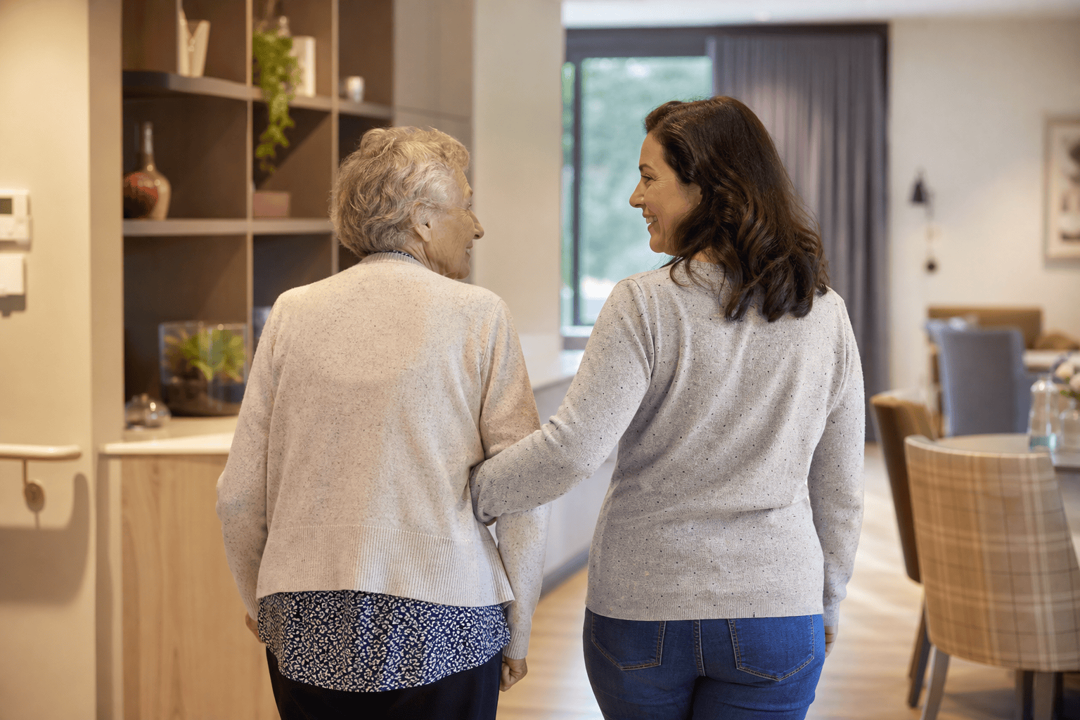 Ältere Person und Angehörige in einem hellen Wohnbereich eines Pflegeheims.