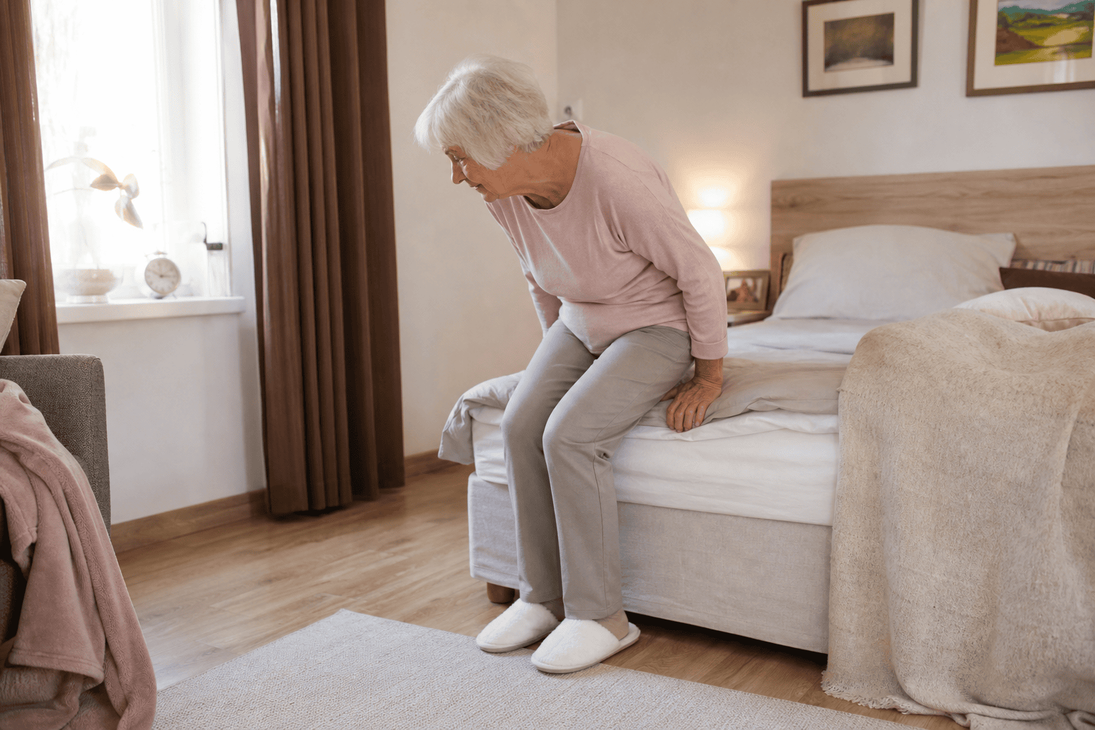 Ältere Frau steht kontrolliert von einem Bett mit passender Sitzhöhe auf